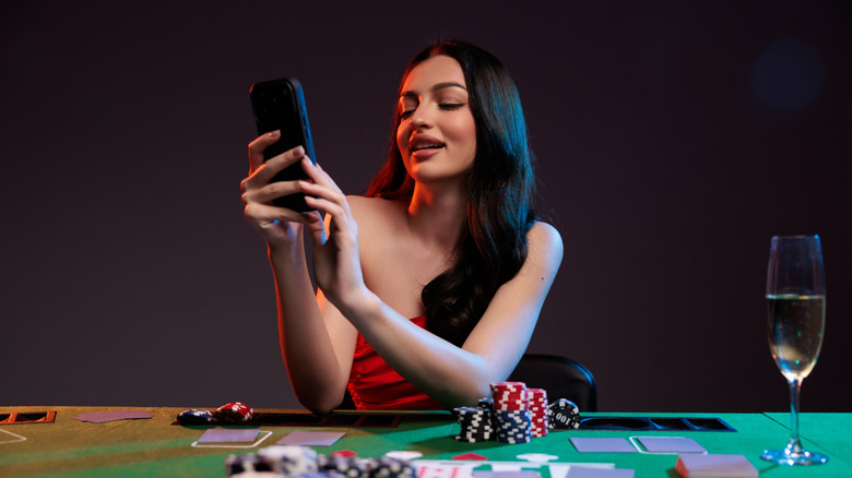 A dark-haired women in a red dress sitting at a poker table holding her cell phone
