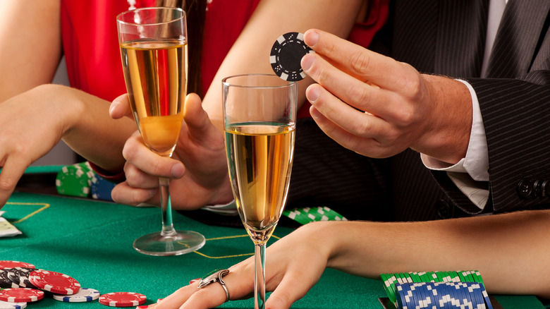 A pair of filled champagne glasses being held at a poker table in a casino
