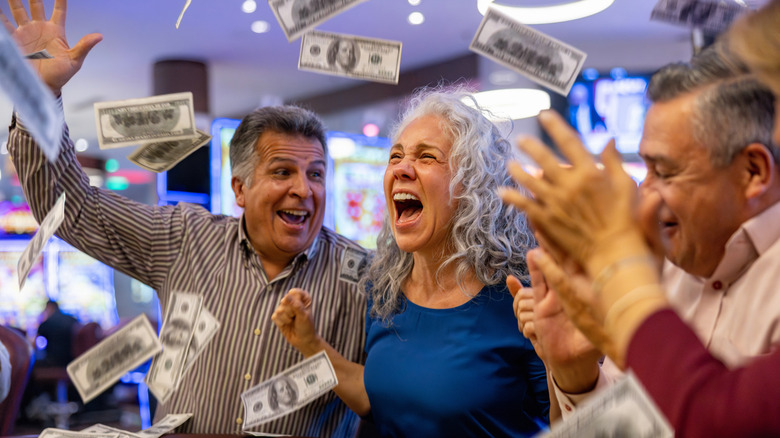 A group of older men and women excitedly throwing dollar bills in the air at a casino