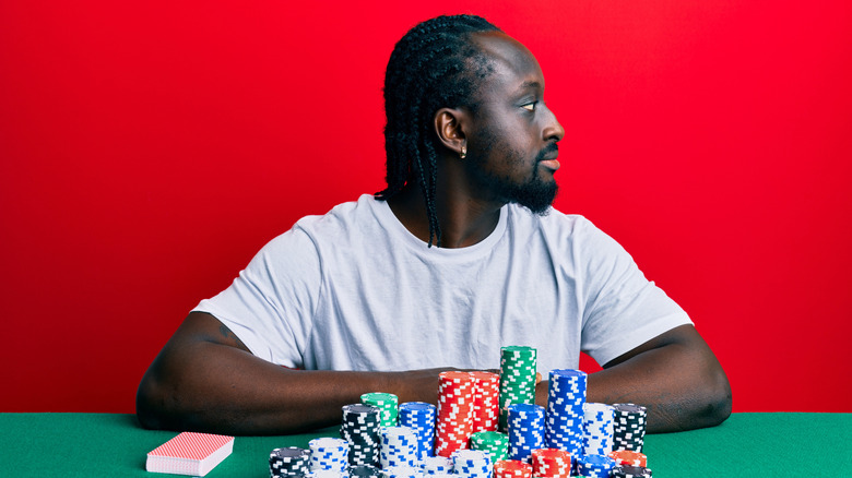 A man looking away from his pile of casino chips and cash on a table