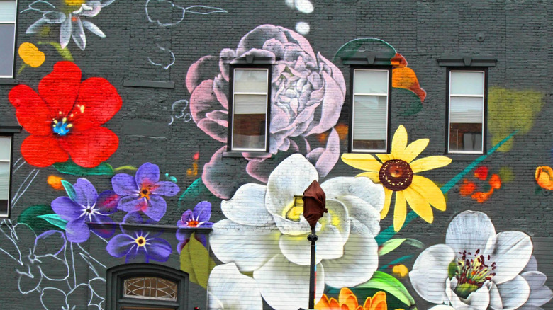 A dark gray wall with huge, bold-colored red, pink, white, yellow, and purple flowers painted across it, part of the Bright Walls mural display.
