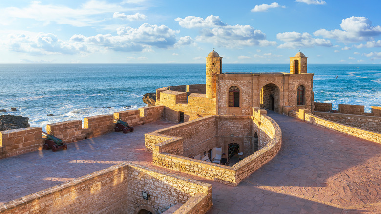 Portion of fortress walls surrounding medina in Essaouira, Morocco, with Atlantic ocean and cloudy blue sky