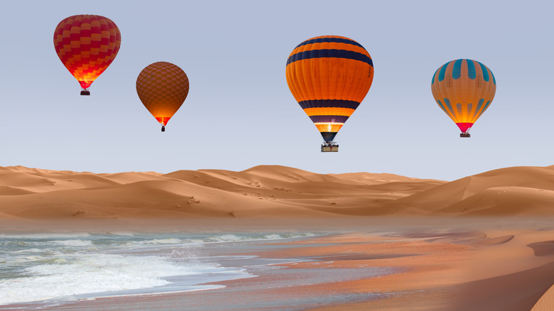 Four hot air balloons over desert dunes and ocean in Namibia.