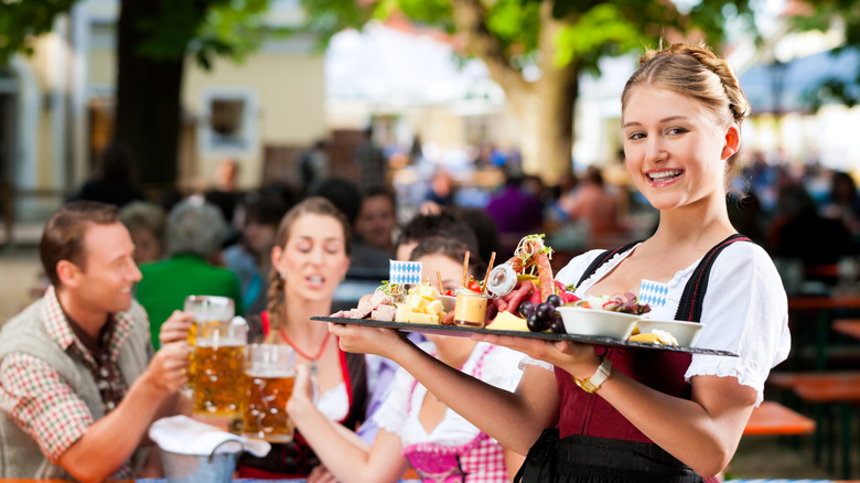 A smiling waitress holding a tray of German food inside a beer garden
