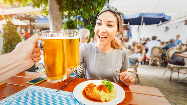 A young woman not making eye contact while clinking her glass of beer at a beer garden