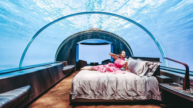 A woman in a pink dress posing on a bed in an underwater hotel room at The Conrad Maldives on Rangali Island