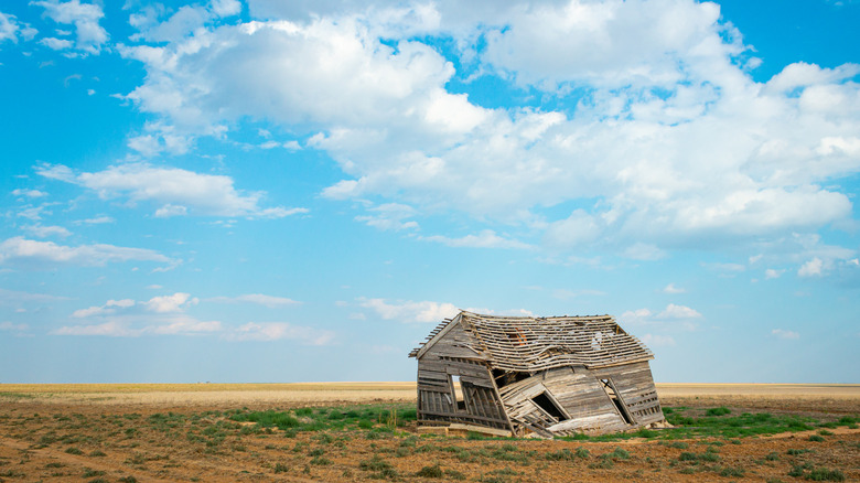 A dilapidated farmhouse on an open Oklahoma prairie under a partly cloudy sky