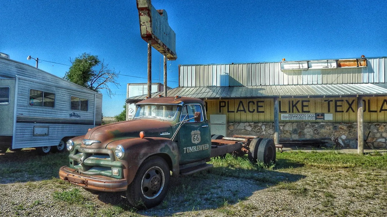An old, rusting truck without a bed sitting in front of a dilapidated, abandoned bar