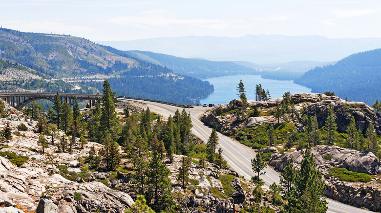 The historic Donner Pass Road in the Sierra Nevadas surrounded by pine trees and boulders with a view of the bridge and Donner Lake in the distance.