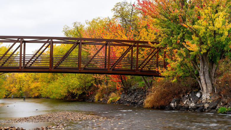 a red steel bridge over a river with fly fishers in the backround and fall foliage
