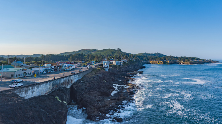 A rocky coastline with waves crashing on the shore and a town overlooking the ocean