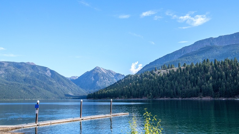 A dock jutting out into a pristine lake with forested mountains in the backgorund