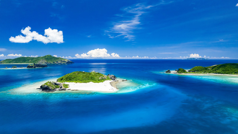 A trio of remote white sand ilsands with greenery against deep blue waters