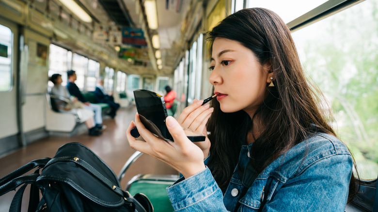 Young woman putting on lipstick on the train