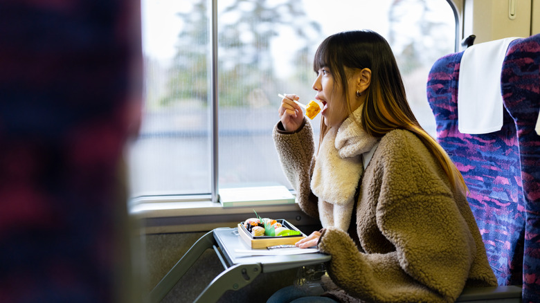 A young woman eating a bento box on the train