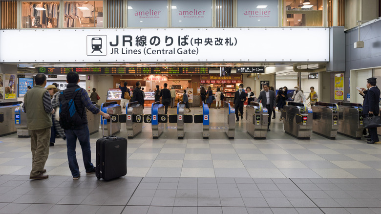 Man holding a suitcase in front of train station's entrance in Japan