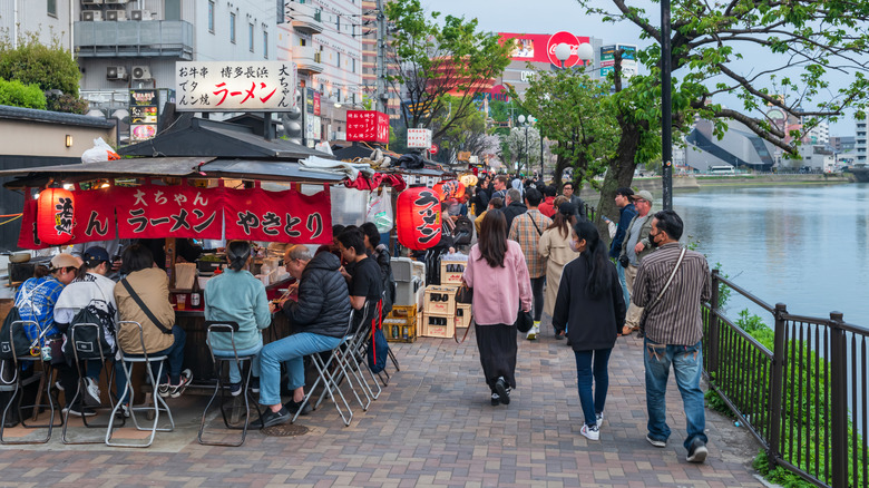 people browsing and eating at food stalls by the river