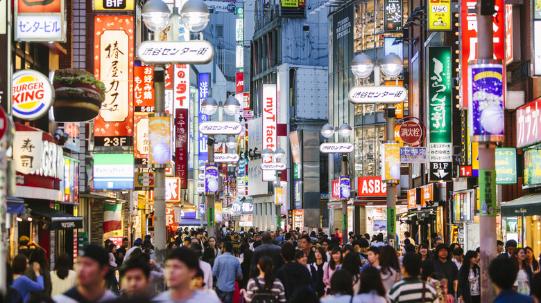 crowds of people in a dense urban street with neon signs