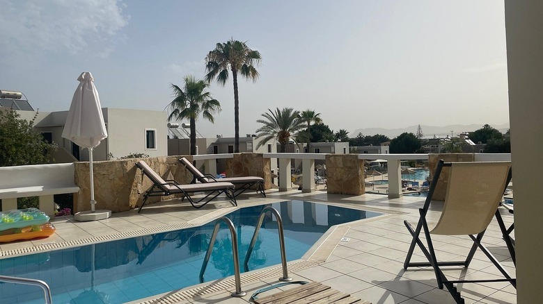 A pool surrounded by beach loungers, pool floaties, and an umbrella at Sirios Village Hotel in Crete