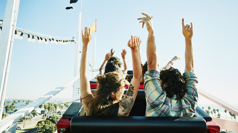 Two people seated on a roller coaster with their arms in the air