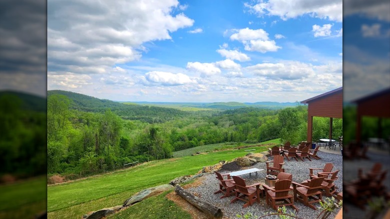 Grass and tree-covered hills stretching into the horizon with a gravel area and chairs in the lower-right corner.