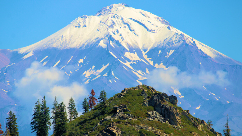 A snow-capped Mounta Shasta with a grass-covered peak in the foreground as seen from Castle Crags State Park