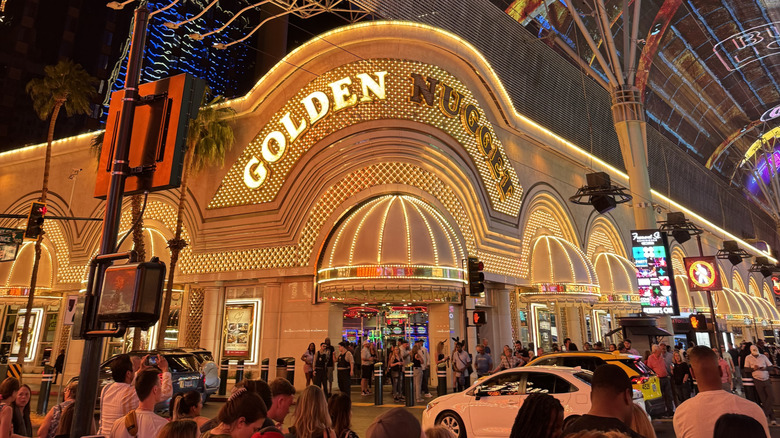 Exterior view of the Golden Nugget casino on Fremont Street at night with crowds of people and cars passing by