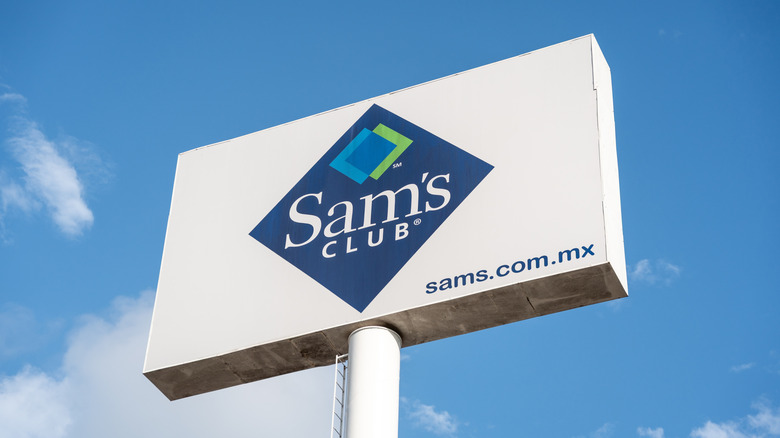 An outdoor Sam's Club signboard against a lightly cloudy blue sky.