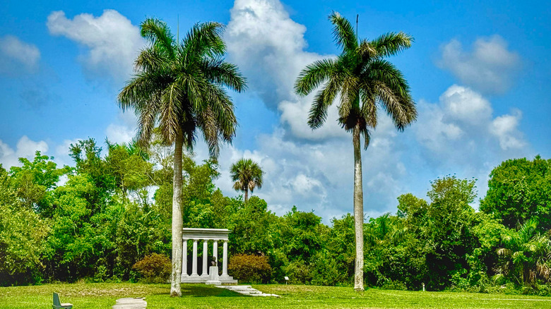 Two palm trees stand out against a green forest and a blue sky with a row of Greek columns in the background at Collier-Seminole State Park in Florida.