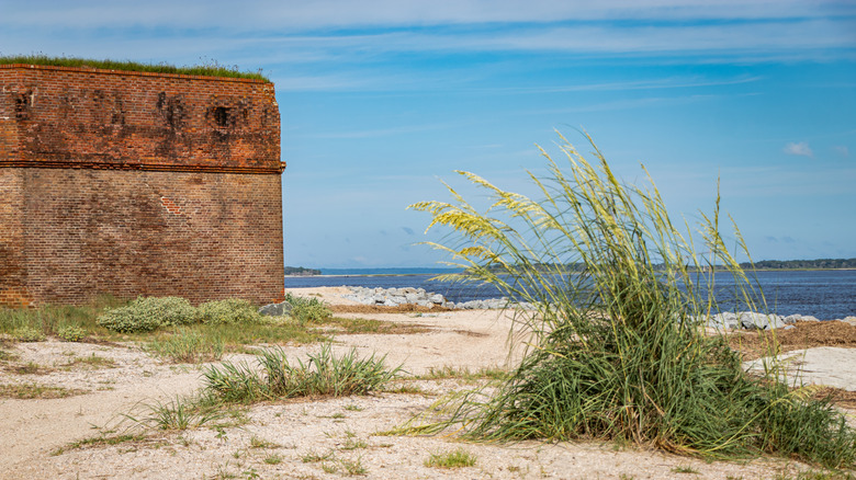 The brick side of Fort Clinch State Park in front of a blue ocean with grasses and white sand and a blue sky.