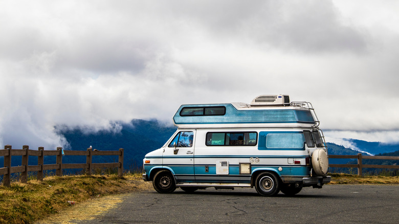 a blue and white RV parked at an overlook surrounded by fog.