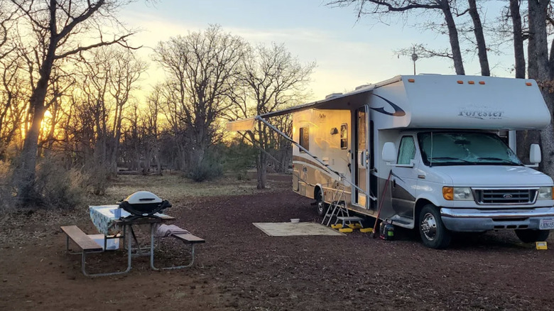 RV with its awning extended parked next to a picnic table with a small grill.