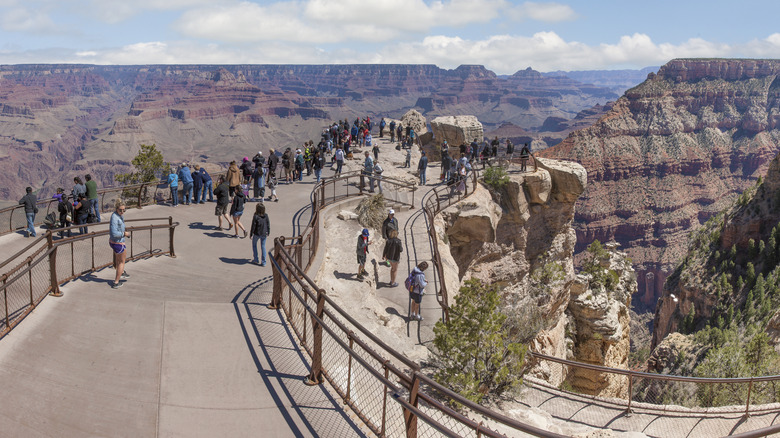 People walk along Mather Point at the South Rim of the Grand Canyon on a clear day