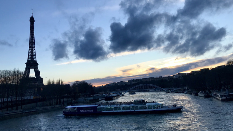 View of the silhouetted Eiffel Tower in the distance and a tourist boat on the Seine at Golden Hour from the Pont de Bir-Hakeim