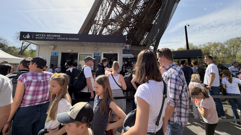 Group of tourists of varying ages waiting in a crowded security queue to enter the base of the Eiffel Tower