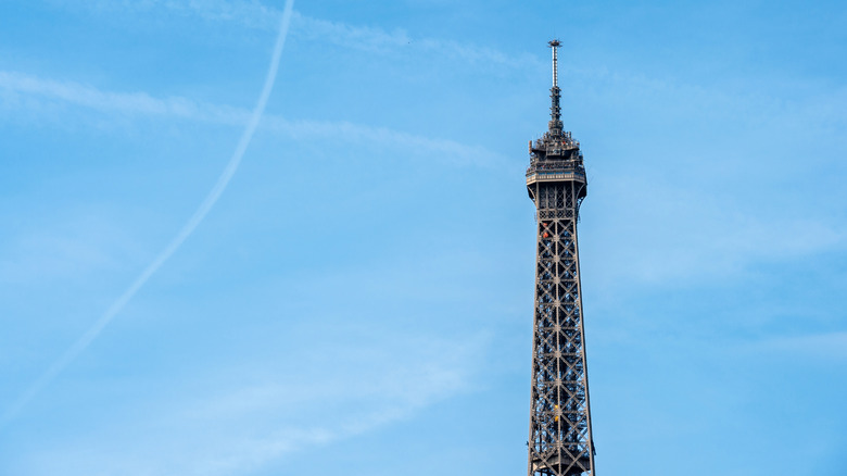 Eiffel Tower summit detail against blue sky with plane traces on clear sky
