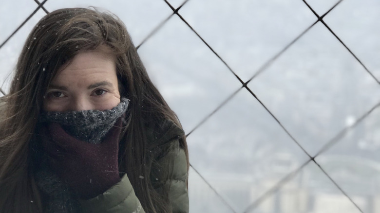 Brunette woman wearing winter clothes in the snow at the top of the Eiffel Tower with obscured view of ground below