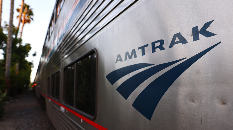 Close-up of the logo on a stopped silver Amtrak train at a station in San Juan Capistrano, California