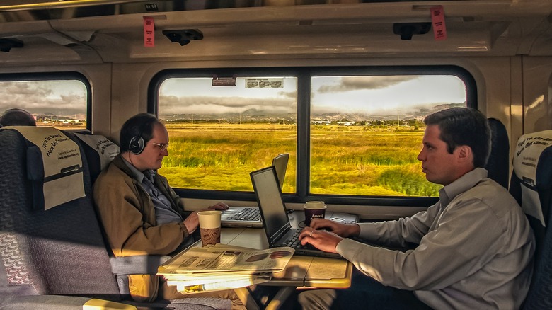 Two Amtrak commuters working on laptops with cups of coffee and newspapers