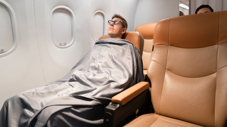 A airplane passenger sleeping under a blanket