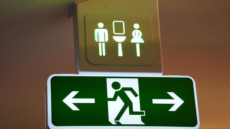 An airplane emergency exit sign next to a restroom sign