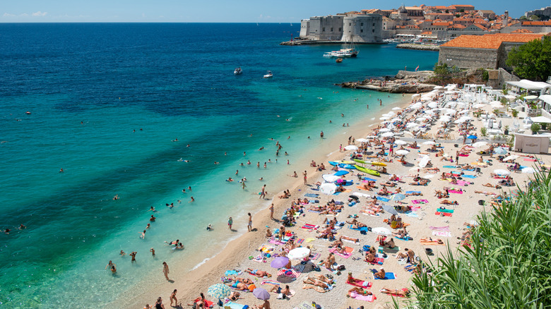 A crowded beach with a view of Dubrovnik's old town
