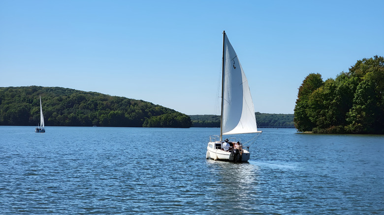 Two sailboats with white sails on Lake Arthur, with treed shoreline in the background under a blue sky