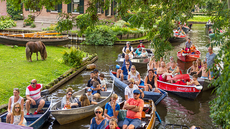 A number of small boats carrying many tourists sailing on a narrow canal