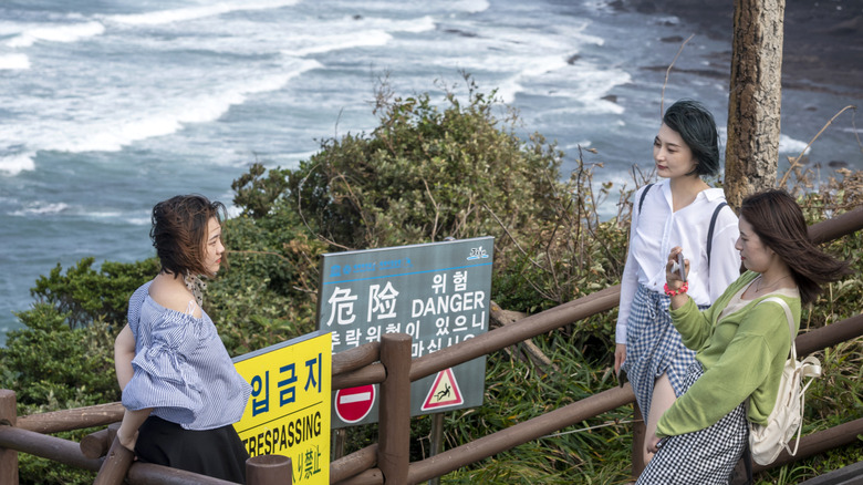 Female Asian tourists taking photos of each other by the beach, 'no trespassing' signs visible