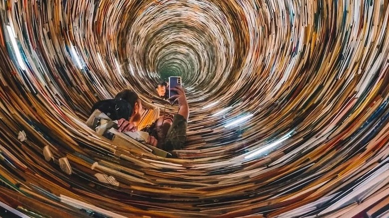 Person inching their phone ahead to take a photo of a vortex lined with books