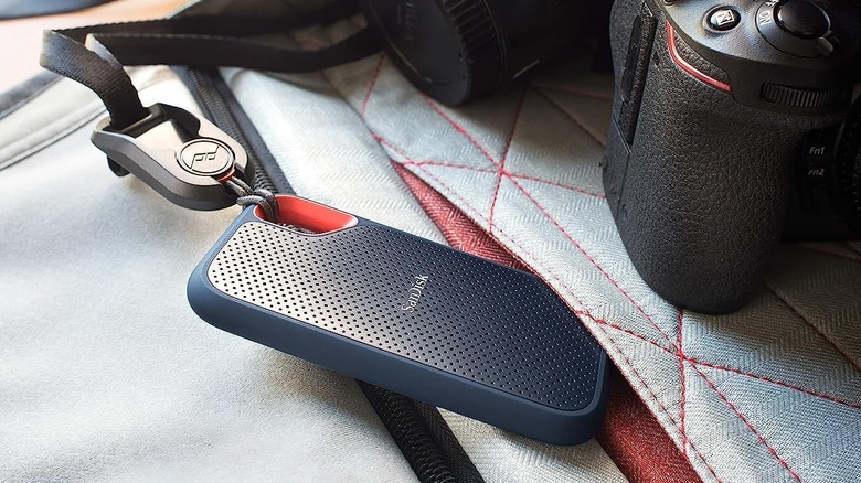 A SanDisk Extreme Portable external hard drive attached to a lanyard, sitting beside a camera