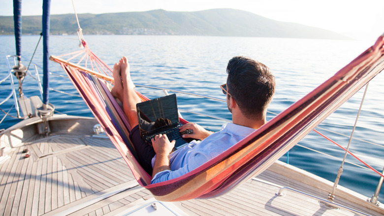 A man lounges in a hammock on a boat with a laptop on his lap