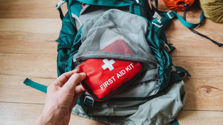 A hand reaches for a bright red first aid kit in a backpack.