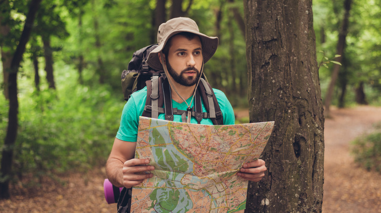 Bearded man holding a map and looking confused in a forest